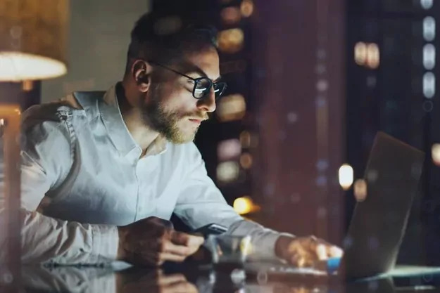 tradutor freelancer sentado segurando um celular e mexendo no notebook após entregar um serviço de tradução