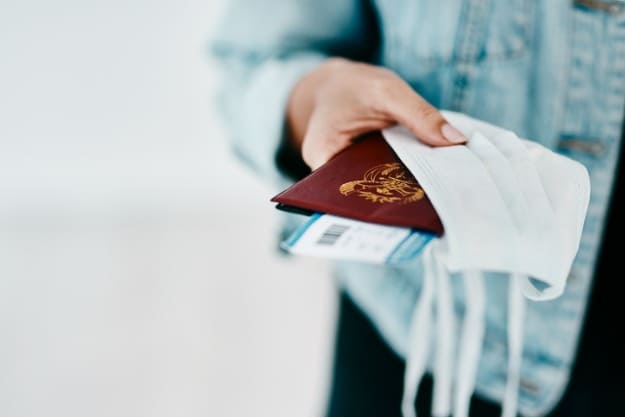 Mão de mulher com passaporte e máscara em mãos.