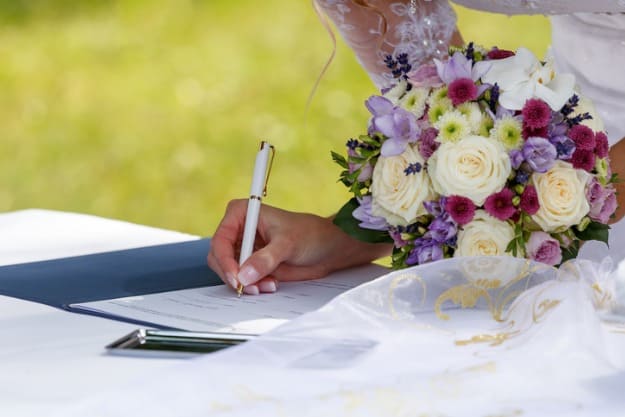 Mulher com buquê na mão assinando certidão de casamento.