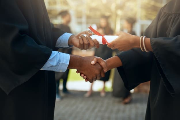Mulher apertando a mão de homem enquanto recebe diploma.