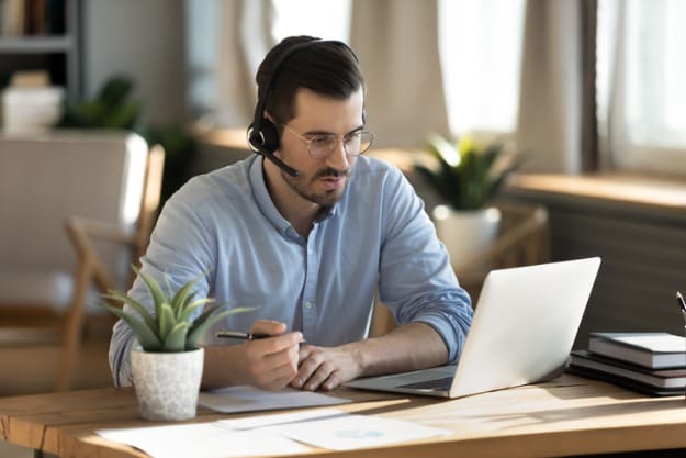 O que é necessário para fazer uma tradução juramentada online Homem sentado em frente ao notebook fazendo anotações para tradução juramentada online