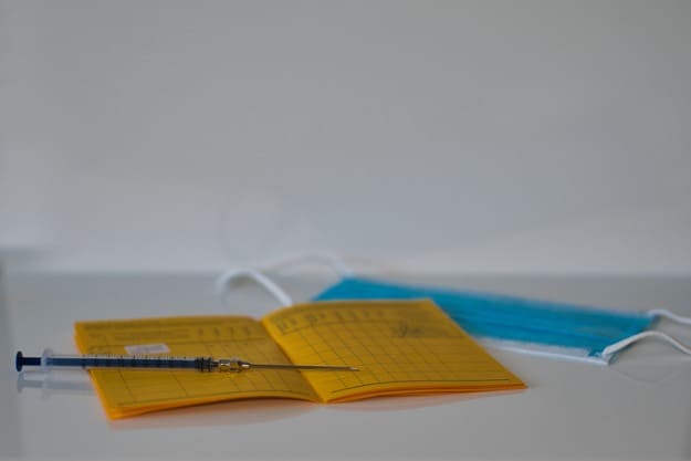Importância da tradução juramentada de carteira de vacinação Carteira de vacinação, máscara e seringa em cima de mesa