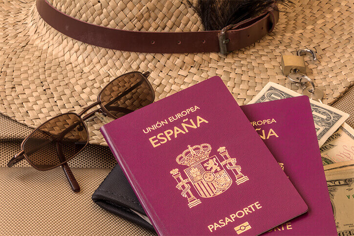 óculos, chapéu, carteira, dinheiro e passaporte espanhol para em cima de uma mesa