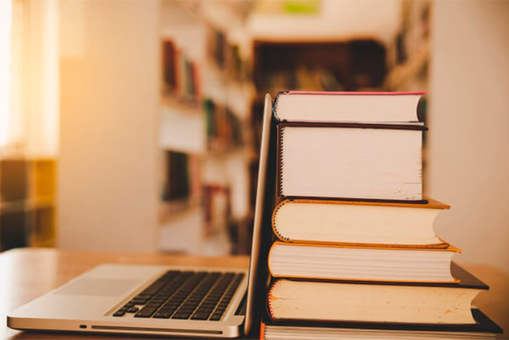 Notebook e uma pilha de livros que ilustram a tradução técnica de artigos científicos