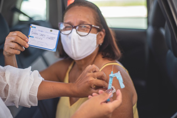 senhora tomando vacina enquanto segura comprovante de vacinação após fazer tradução juramentada.