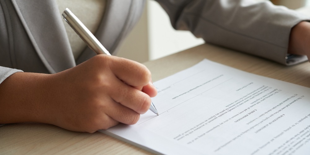 Imagem com foco nas mãos de pessoa escrevendo em papel, representando tradução juramentada